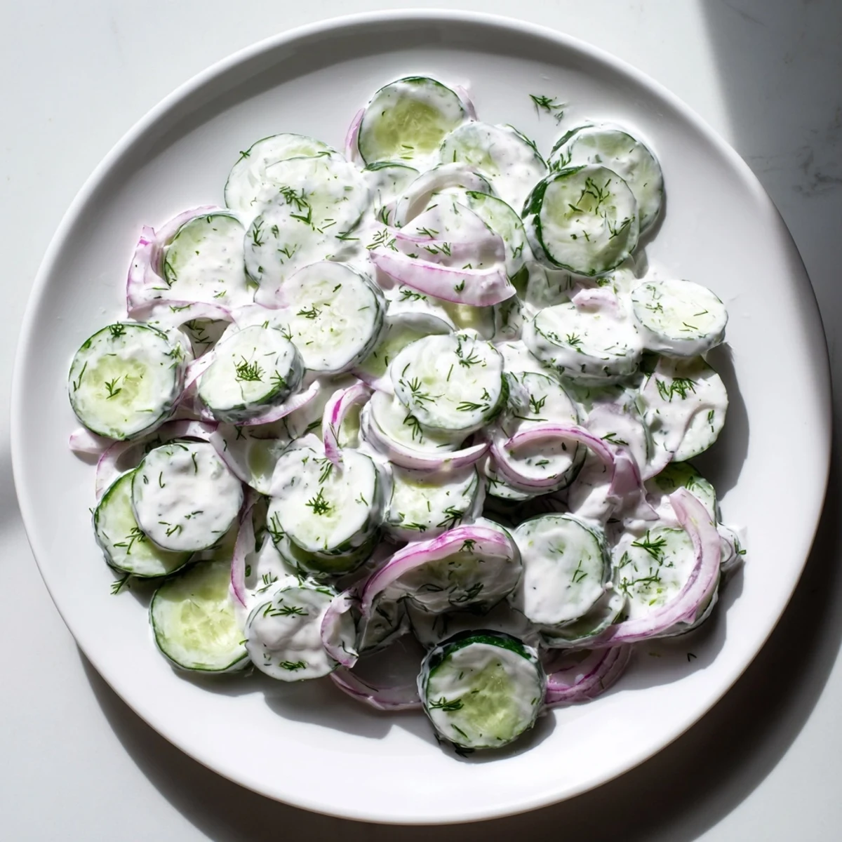 Fresh cucumber dill salad in a white bowl with creamy dressing and red onion slices