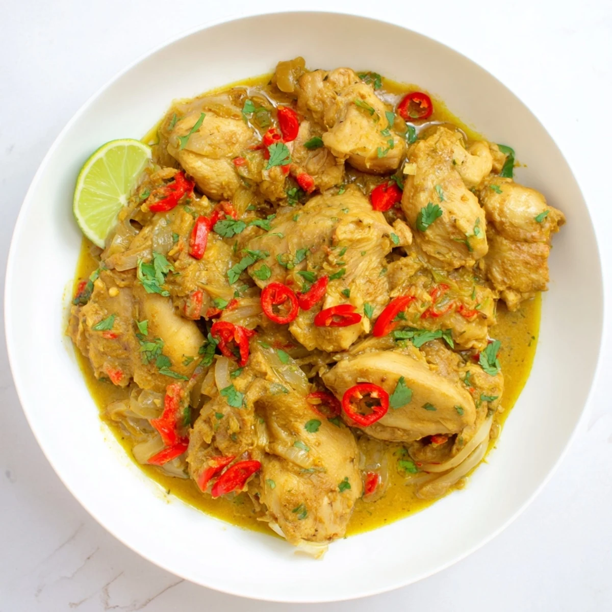 Creamy spicy Brazilian coconut chicken served in white bowl over steaming rice with lime wedges on side