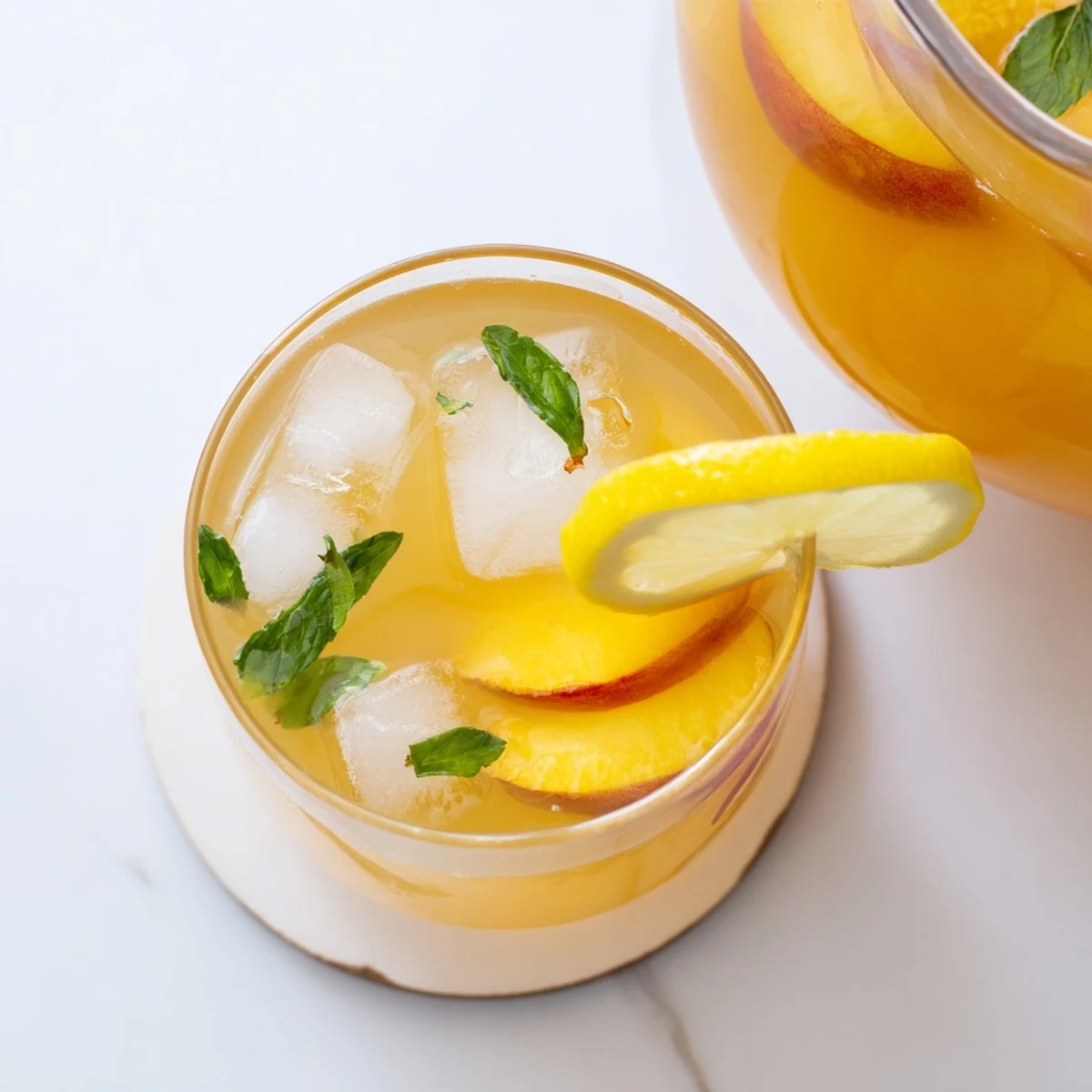 Fresh peach lemonade poured over ice with floating peach slices and lemon wheels on a sunny day