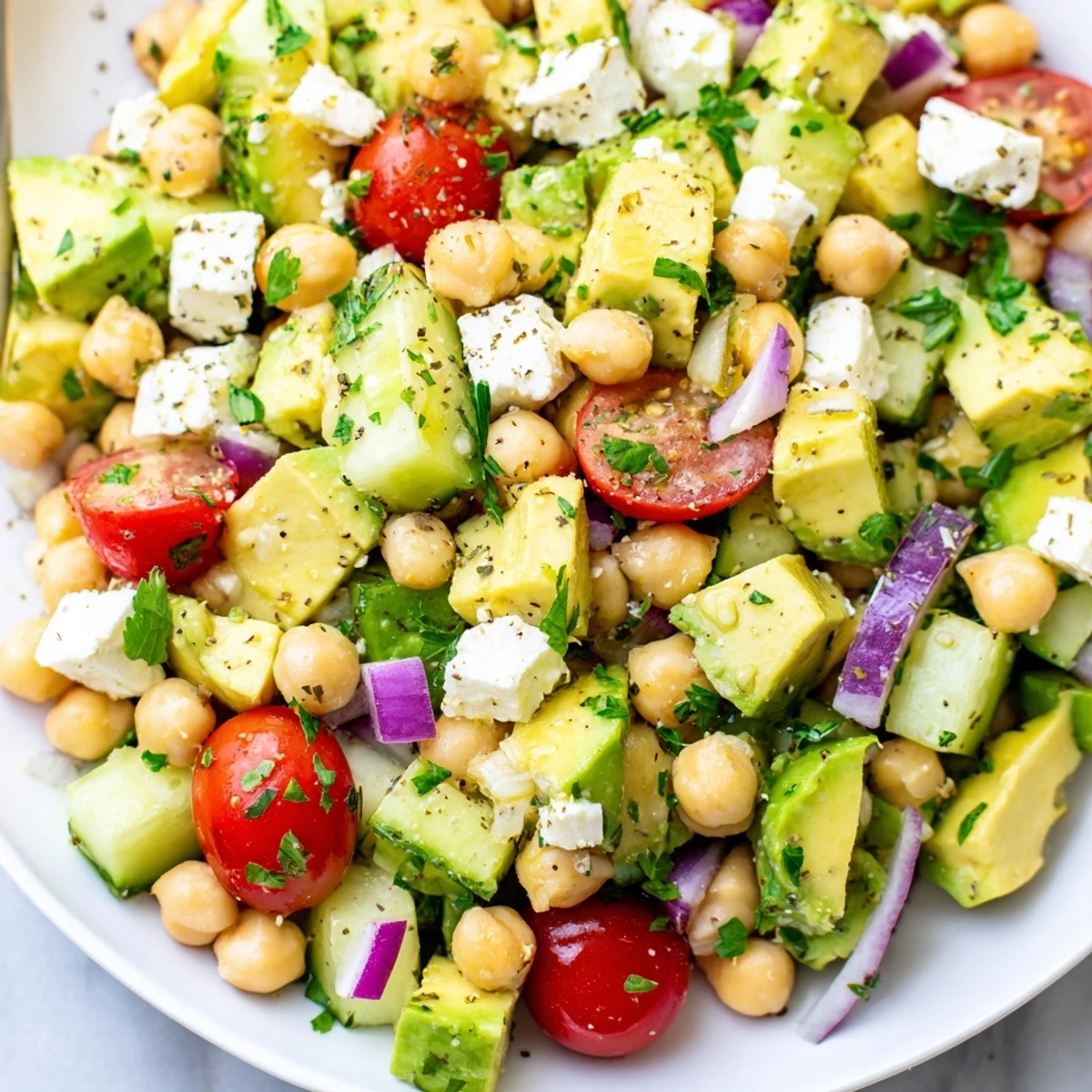 Vibrant chickpea feta avocado salad drizzled with lemon herb dressing on a white platter