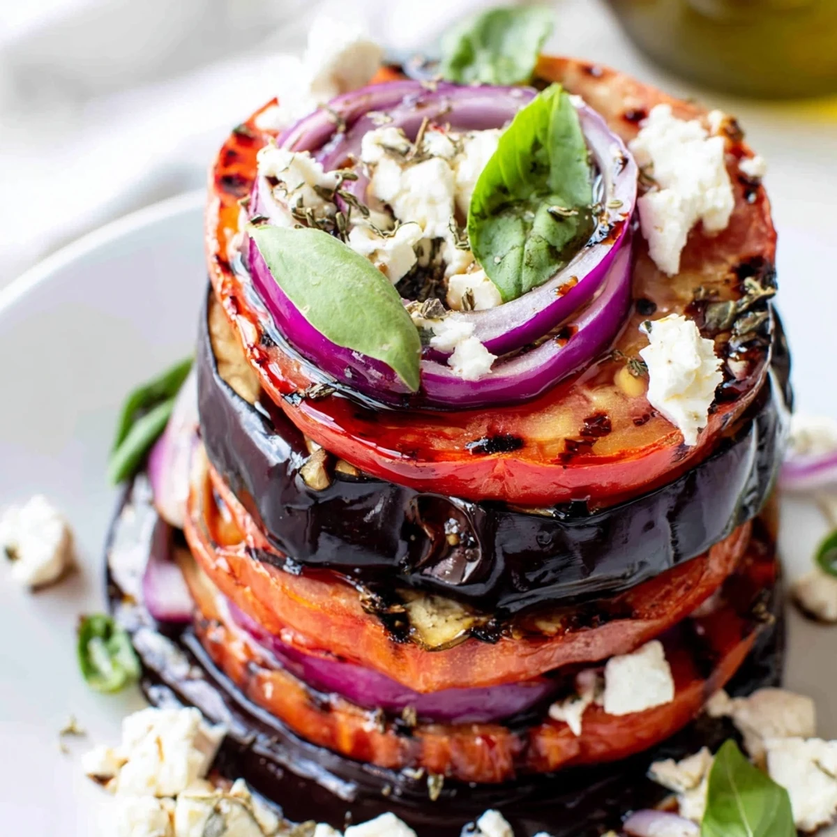 Smoky grilled tomato eggplant stacked on a platter with fresh basil and crumbled feta