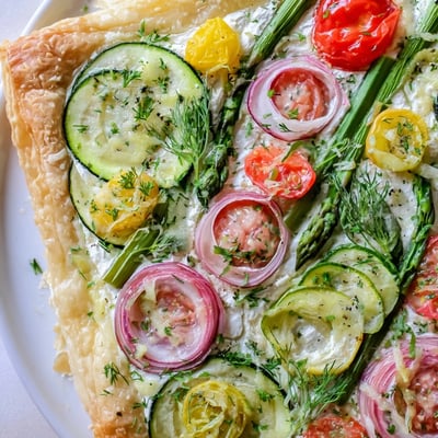A slice of Spring Vegetable Tart with Puff Pastry reveals creamy goat cheese and wilted spinach.