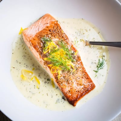 Plated Salmon With Lemon Cream Sauce beside roasted potatoes and bright lemon wedges