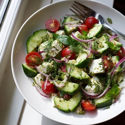 Creamy feta cheese crowning a bed of sliced cucumbers, tomatoes, and fragrant Mediterranean herbs